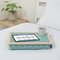 The lap tray in Aqua Marine Spotty is pictured on top of a bed dressed with white bed linen. The tray holds a white mug of coffee, an electronic tablet and a pen. A plant stands on a side table next to the bed.