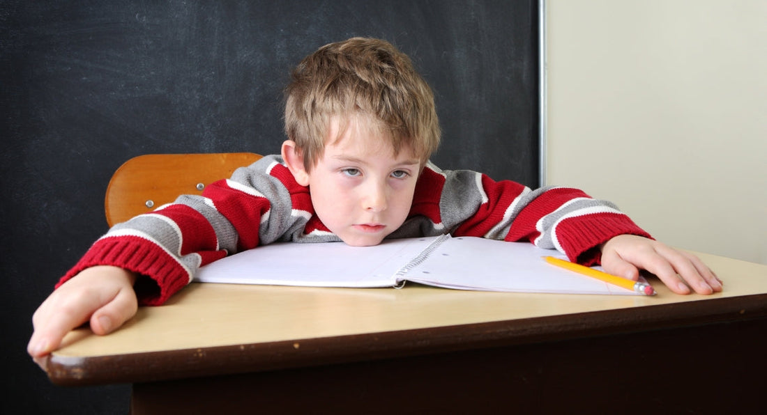 Bored boy resting his head on a school desk over a notebook.