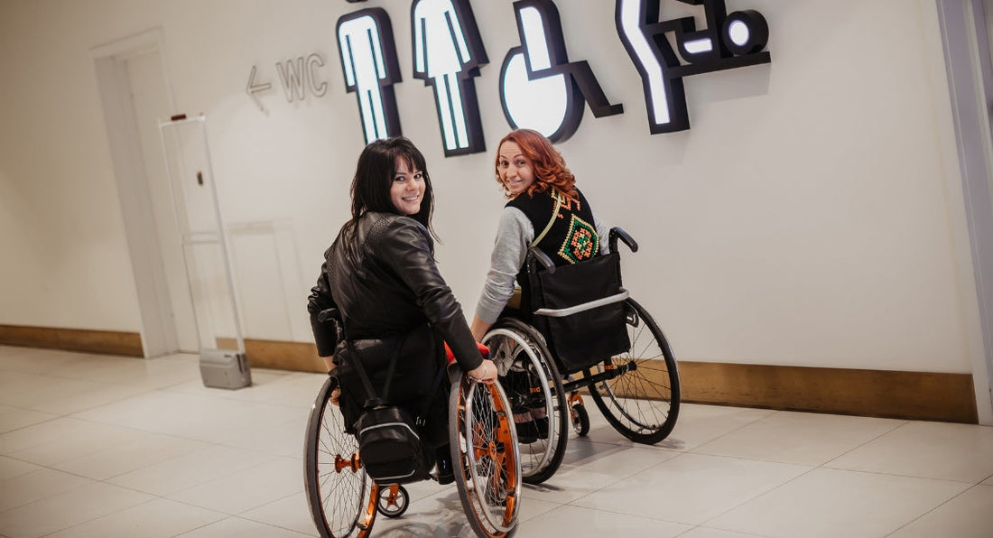 Two women in wheelchairs smile while moving toward public restrooms.