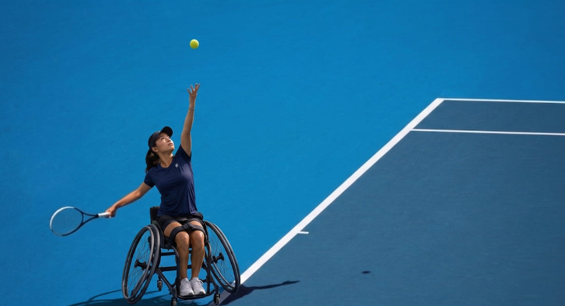 A female wheelchair tennis player serving a ball on a blue court.
