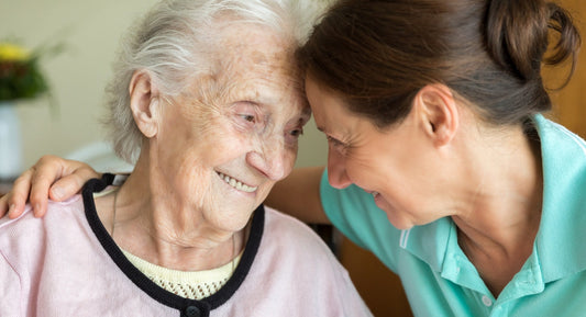 Older woman and caregiver smiling with foreheads touching.