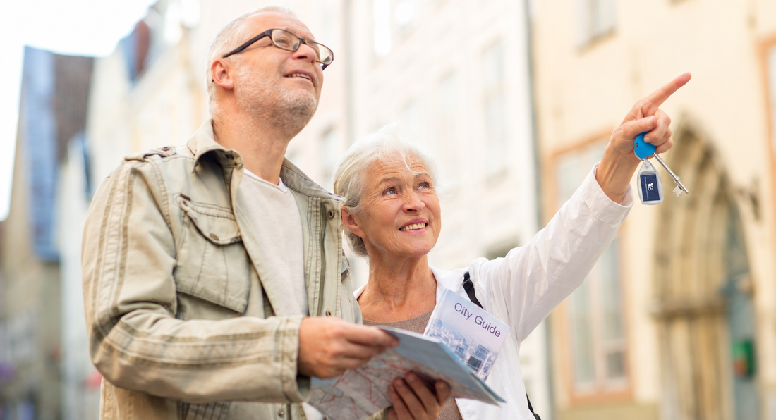 An older couple holding a city guide map, with the woman pointing and holding a key.