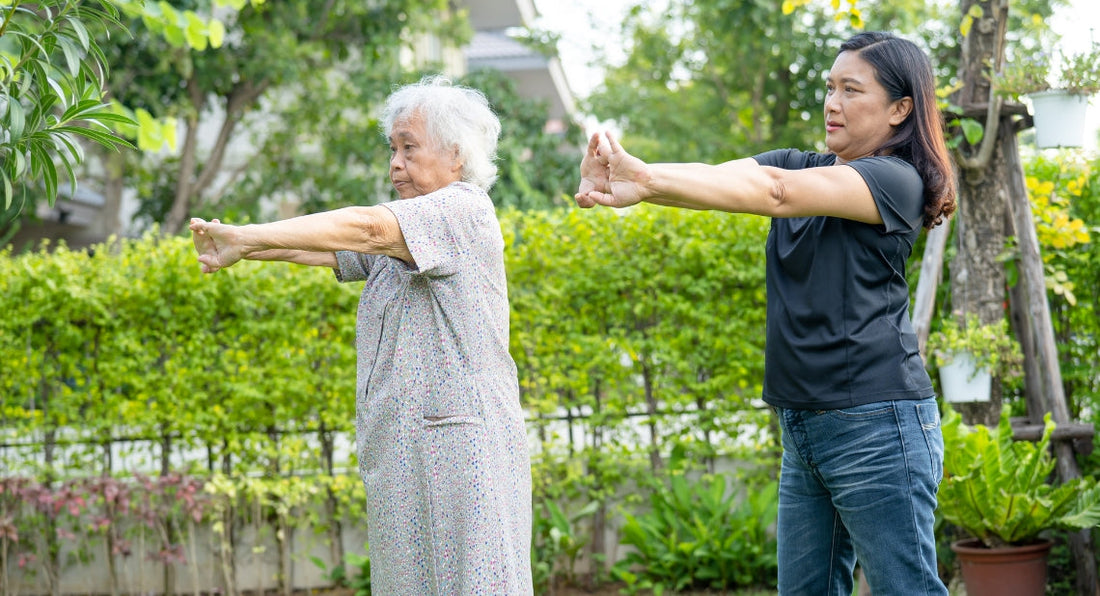 Two women doing arm stretching exercises outdoors.