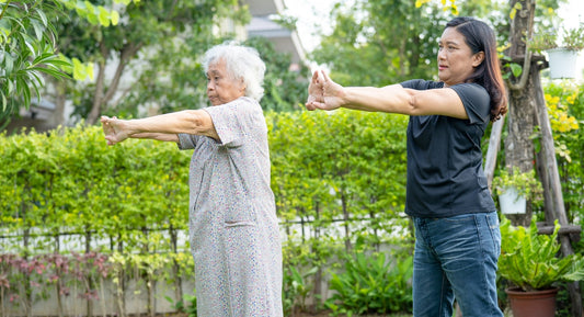 Two women doing arm stretching exercises outdoors.