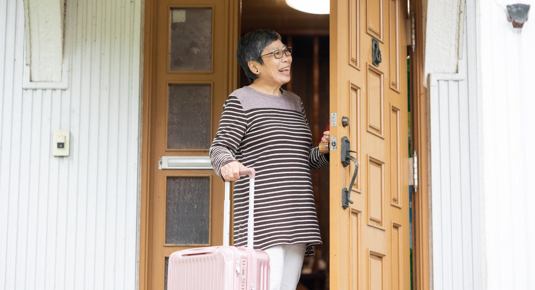 Older woman standing at an open door with a pink suitcase.
