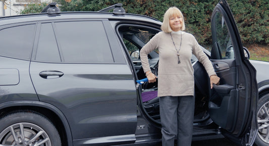 Woman standing next to a car using a blue mobility handle for support.