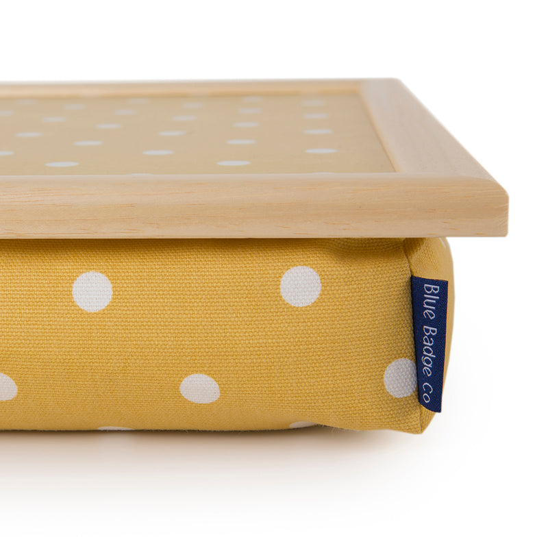 Bean Bag Lap Tray in Canary Yellow Spotty against a white back ground. A close up of the corner of the tray, showing the blue badge company label as well as the quality of the fabric and light wooden edging.