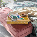 The Canary Yellow Spotty Lap Tray is pictured on a pink velvet ottoman at the foot of a bed. On the tray there are biscuits and an open magazine.