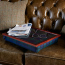 The bean bag lap tray in Blackwatch Tartan is pictured on a brown leather sofa with glasses and a newspaper on top.