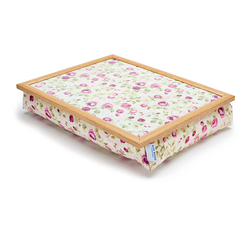 Bean Bag Lap Tray in Mulberry Rose with the Blue Badge Company label showing. The Mulberry Rose fabric depicts delicate dusky pink roses with light olive green leaves on a creamy beige background. The lap tray has a smooth see through laminated top, with a light wooden beaded edge.