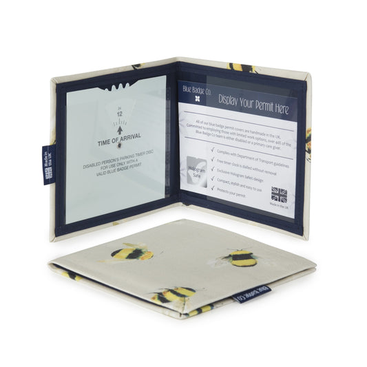 Two Disabled Blue Badge Wallets in Busy Bees fabric are pictured. One stands open showing clock display on left behind plastic window, with room to adjust time dial. On the right is a card insert showing place for permit and a hologram safe design. Second, closed wallet lays in front of the open wallet to display fabric. The Busy Bees fabric has a pattern of black and yellow bumble bees with delicate white wings, on a cream background.