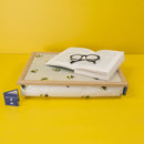 The Busy Bees Lap Tray with a bright yellow background. On the tray rests an open book, held open with a pair of closed reading glasses. There is a Blue Badge Company care instructions tag next to the tray. 