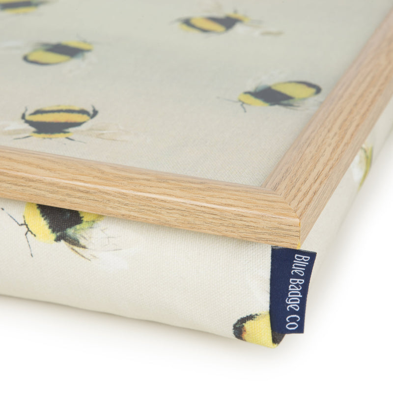 A close view of the corner of the lap tray, showing the wooden lip around the top of the tray, the quality Busy Bees print fabric, and the Blue Badge Company label.