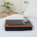 The bean bag lap tray in Blackwatch Tartan is pictured on top of a bed dressed with white bed linen. The tray holds a white mug of coffee, an electronic tablet and a pen. A plant stands on a side table next to the bed.
