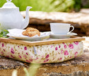 Bean Bag lap tray in Mulberry Rose fabric sits on a wall in a garden, it holds a tea pot, tea cup and saucer, and a plate of biscuits.