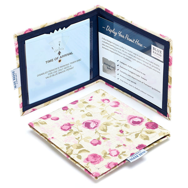 Two Disabled Blue Badge Wallets in Mulberry Rose fabric are pictured. One stands open showing clock display on left behind plastic window, with room to adjust time dial. On the right is a card insert showing place for permit and a hologram safe design. Second, closed wallet lays in front of the open wallet to display fabric.  The Mulberry Rose fabric depicts delicate dusky pink roses with light olive green leaves on a creamy beige background.