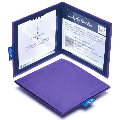 Two Disabled Blue Badge Wallets in Purple Drill fabric are pictured. One stands open showing clock display on left behind plastic window, with room to adjust time dial. On the right is a card insert showing place for permit and a hologram safe design. Second, closed wallet lays in front of the open wallet to display fabric. The Purple Drill fabric is a bright bold block colour.