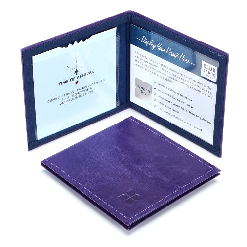 Two Disabled Blue Badge Wallets in purple leather are pictured. One stands open showing clock display on left behind plastic window, with room to adjust time dial. On the right is a card insert showing place for permit and a hologram safe design. Second, closed wallet lays in front of the open wallet. The leather is a rich Purple colour embossed in the bottom right corner with a discreet Blue Badge Co logo.