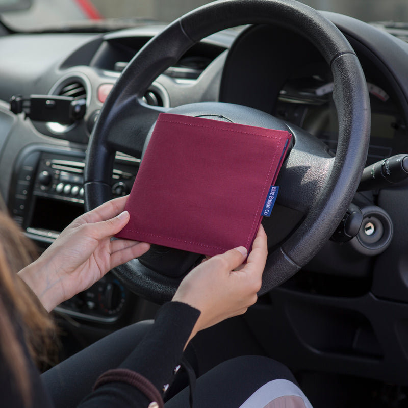 Blue Badge Wallet in Burgundy Panama fabric is held in two hands against a steering wheel.