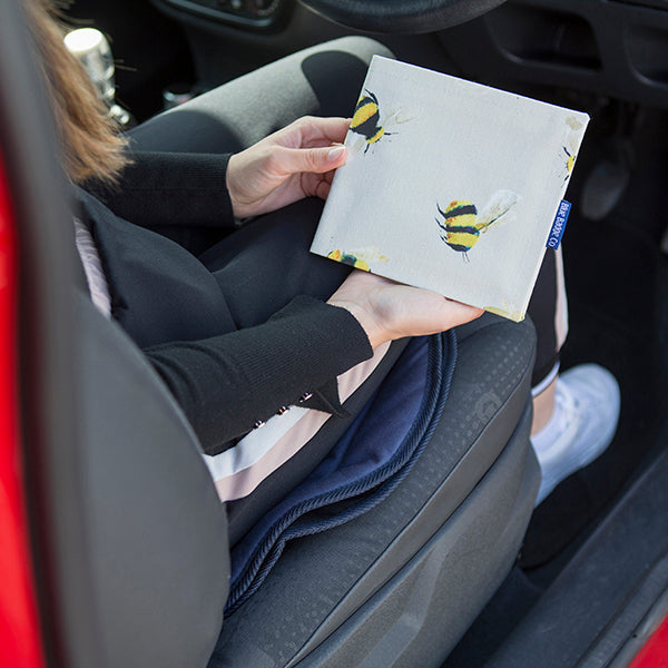 The Blue Badge Wallet in Busy Bees fabric is held in two hands, to the side of a figure seated in the front seat of a vehicle.