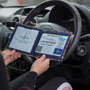 Open Disabled Blue Badge Wallet held in two hands against a steering wheel. The adjustable timer display clock is on the left. On the right is a Devon County Council Disabled Parking Permit with hologram. The acetate window doesn't cover the hologram.