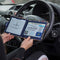 Open Disabled Blue Badge Wallet held in two hands against a steering wheel. The adjustable timer display clock is on the left. On the right is a Devon County Council Disabled Parking Permit with hologram. The acetate window doesn't cover the hologram.