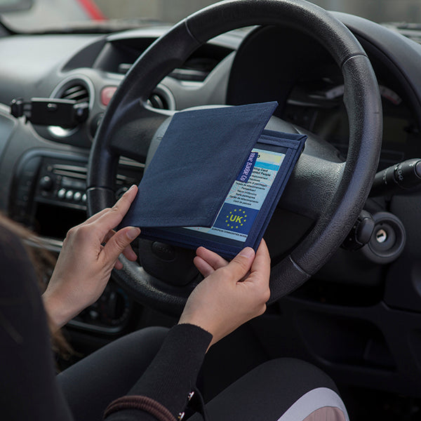 The Blue Badge Wallet is held slightly open, in two hands, against a steering wheel.