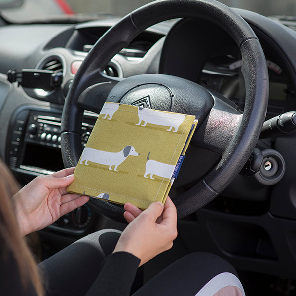 Blue Badge Wallet in Sausage Dog fabric is held in two hands against a steering wheel.